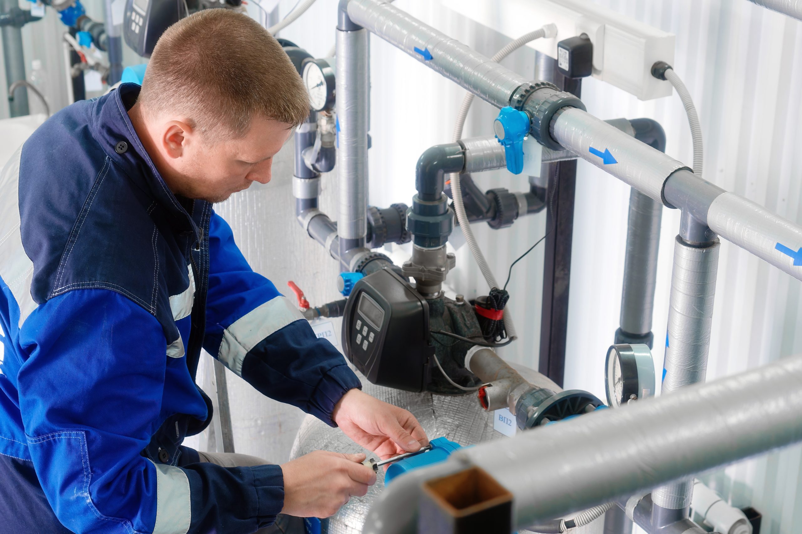 Worker indoors with pipes repairs industrial water supply system. Water supply diagnostics. Authentic workflow.